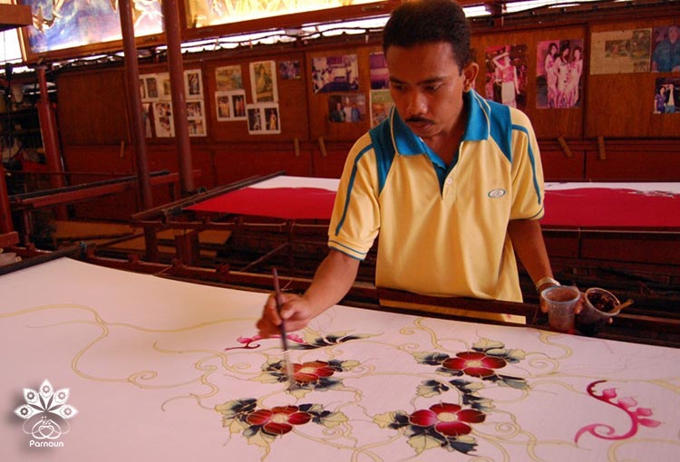  هنرمند مالزیایی در حال ایجاد چاپ باتیک با قلم‌مو بر روی پارچه